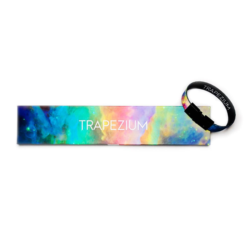 Studio image of Trapezium clasped together laying on the box it comes in, which has a design of a multi-colored light space background and Trapezium centered in white text