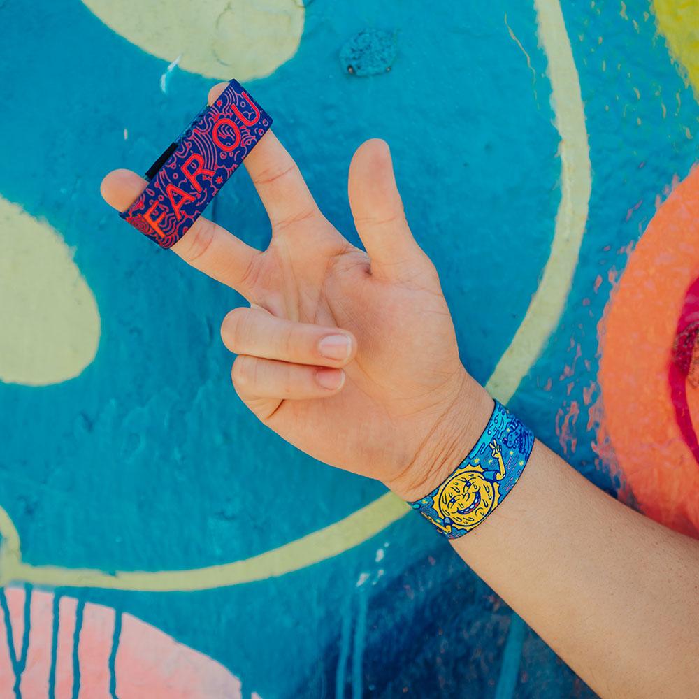 Life style image of Far Out on someone's wrist and 1 Far Out on the middle and pointer finger as the hand makes a peace sign.