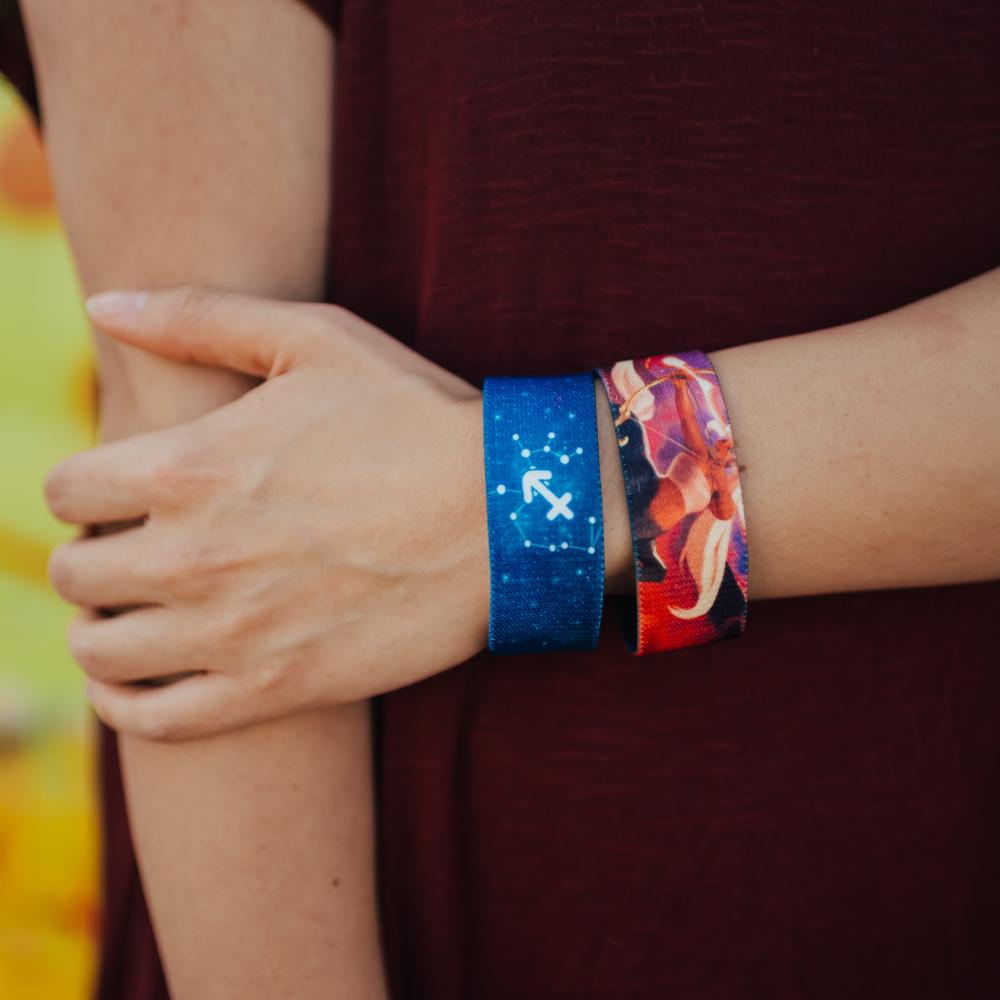 Lifestyle close up image of someone holding their arm and wearing 2 Sagittarius straps on their wrist