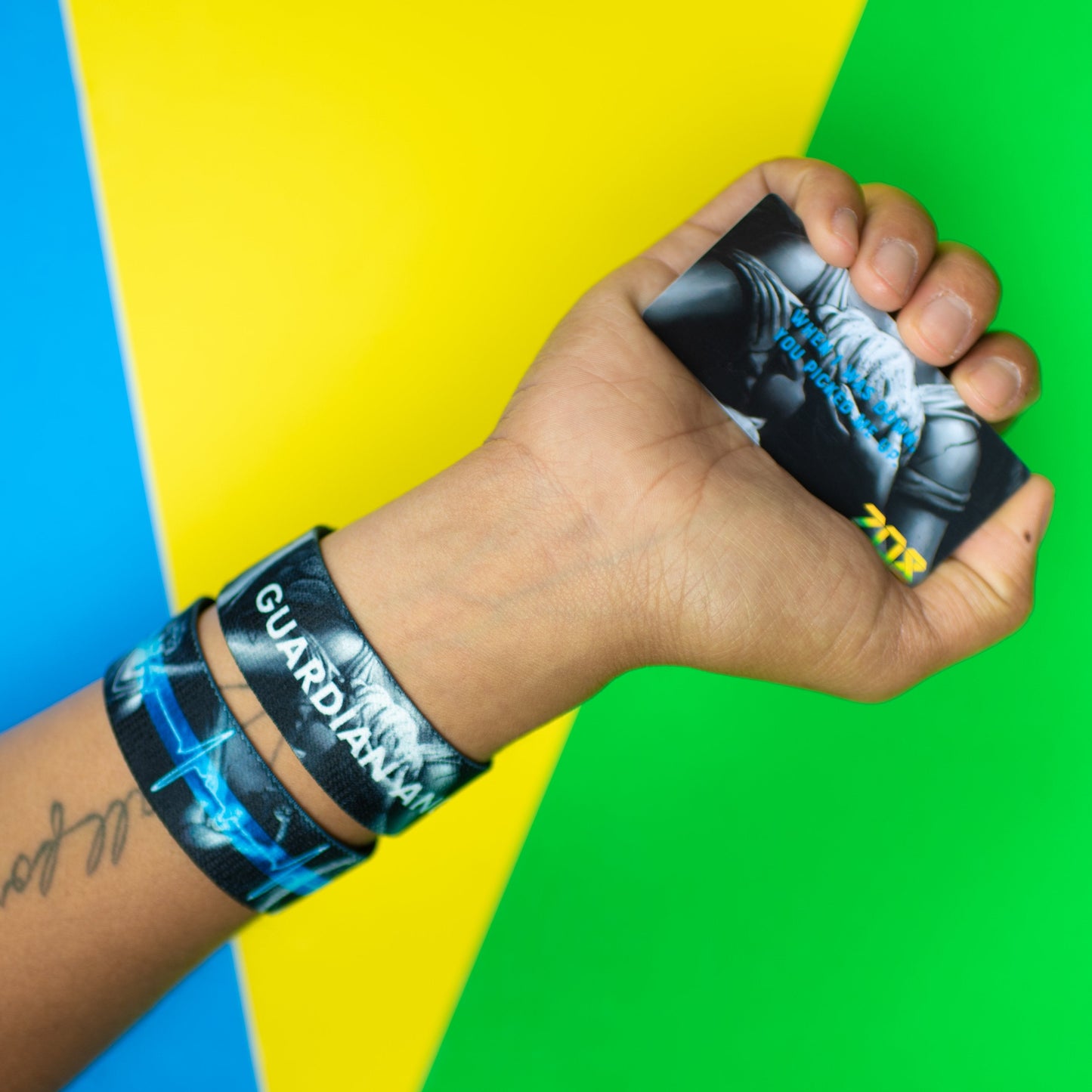 Studio Image of hand holding card that says Guardian Angel with 2 Guardian Angel straps on their wrist