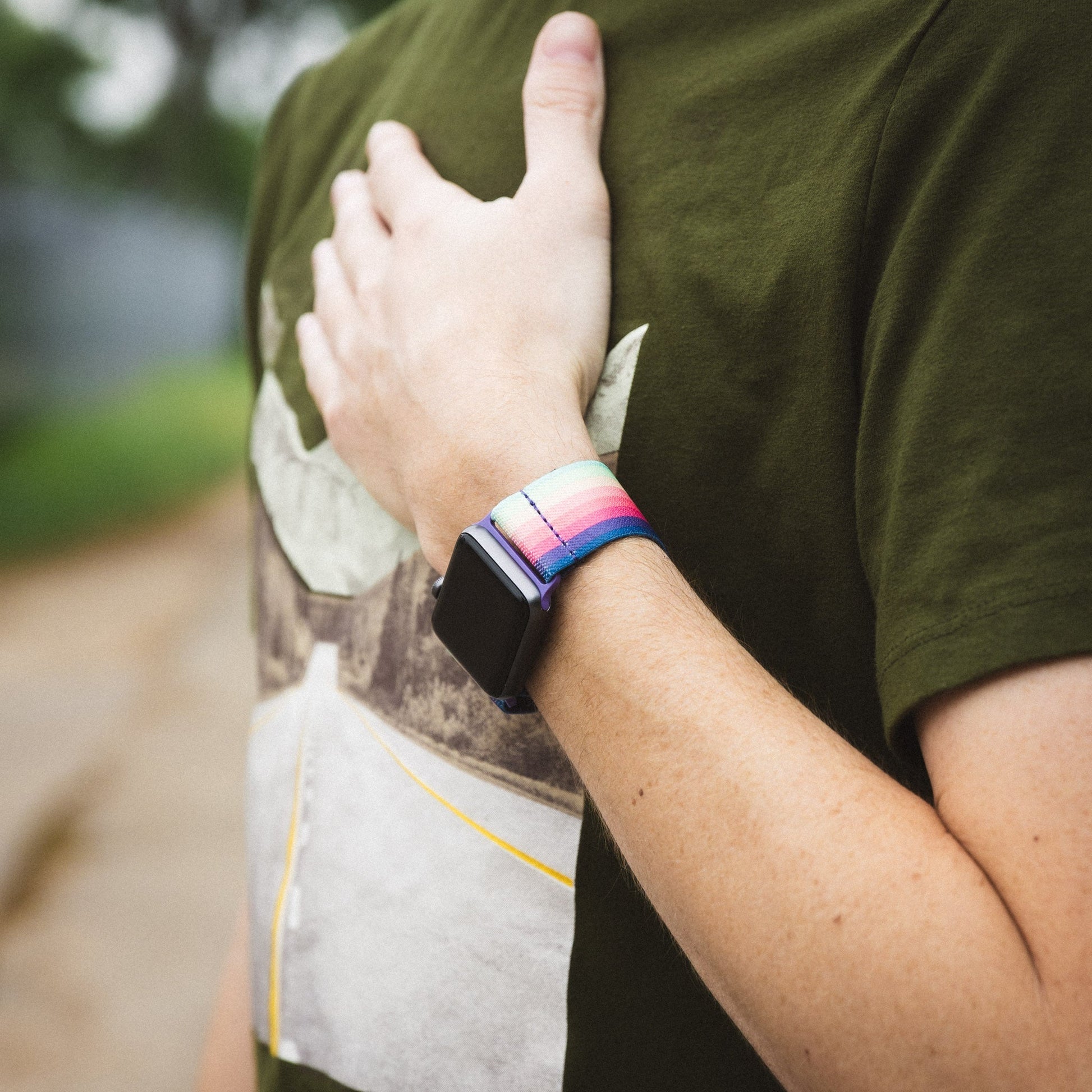 This is a lifestyle photo of a person wearing the watchband on an Apple watch. They have on a green tshirt and have their hand on their heart. 
