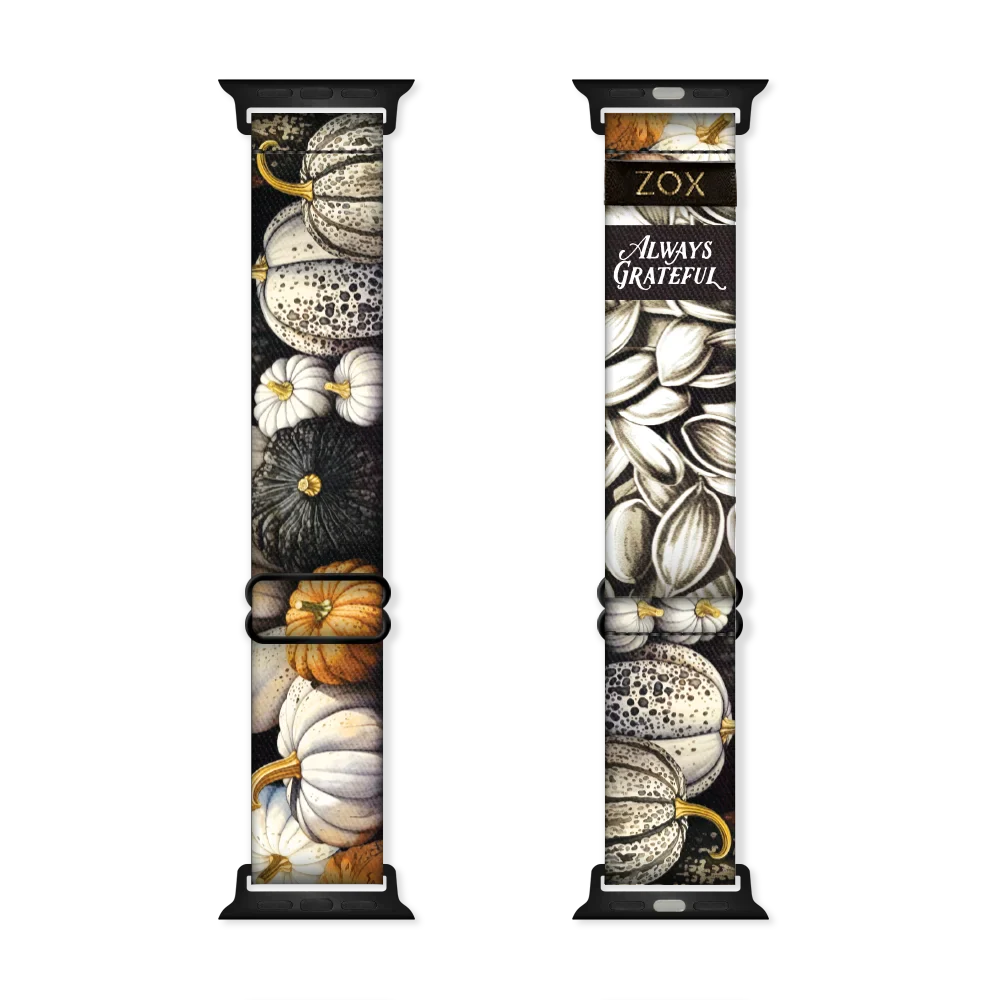 This is a watchband that has pumpkins on the outside in white, grey, black and burnt orange colors. The inside has pumpkin seeds and says Always Grateful. 