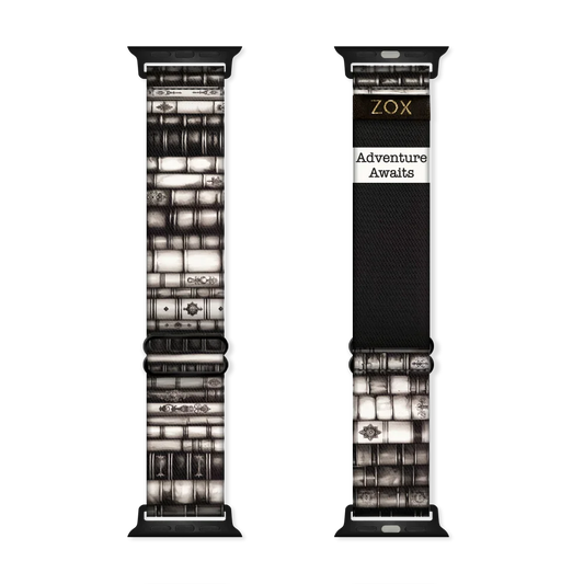 Watchband that is ornate books stacked on top of each other in various shades of black and white. The inside is the same and reads Adventure Awaits. 