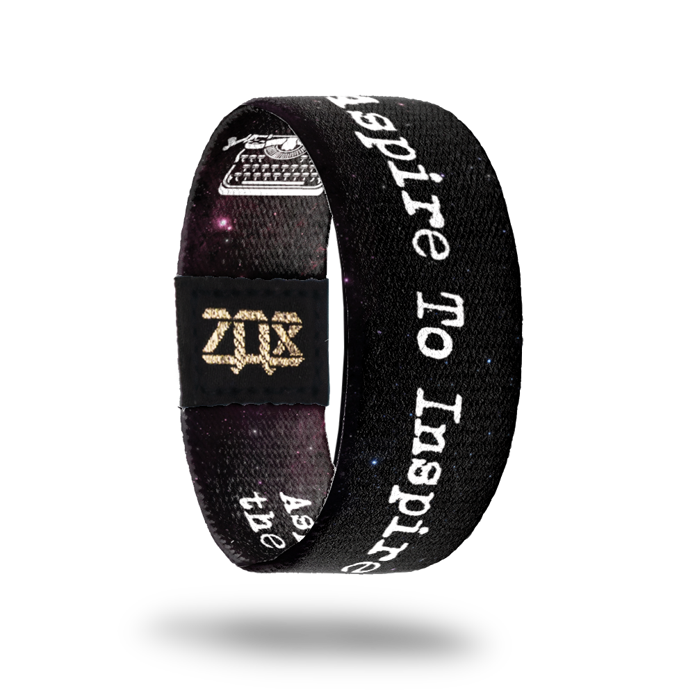 Inside design of Aspire To Inspire has a dark black and bits of purple space background with Aspire To Inspire in white text in the center with a pink nail sized image of a black and white typewriter next to the word inspire