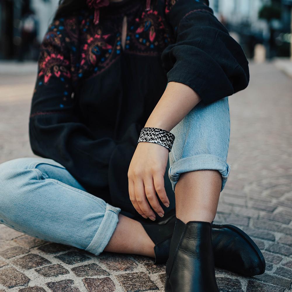 Lifestyle image of someone sitting legs crossed and arm wearing Do wristband is resting on one leg