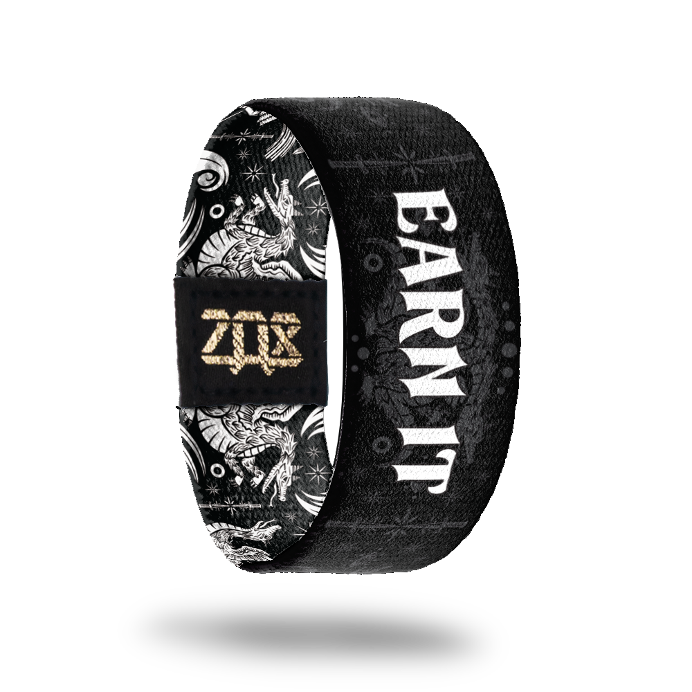 Inside Design of Earn It: black strap with grey design of two headed beast being slayed by knights with white text 'Earn It'