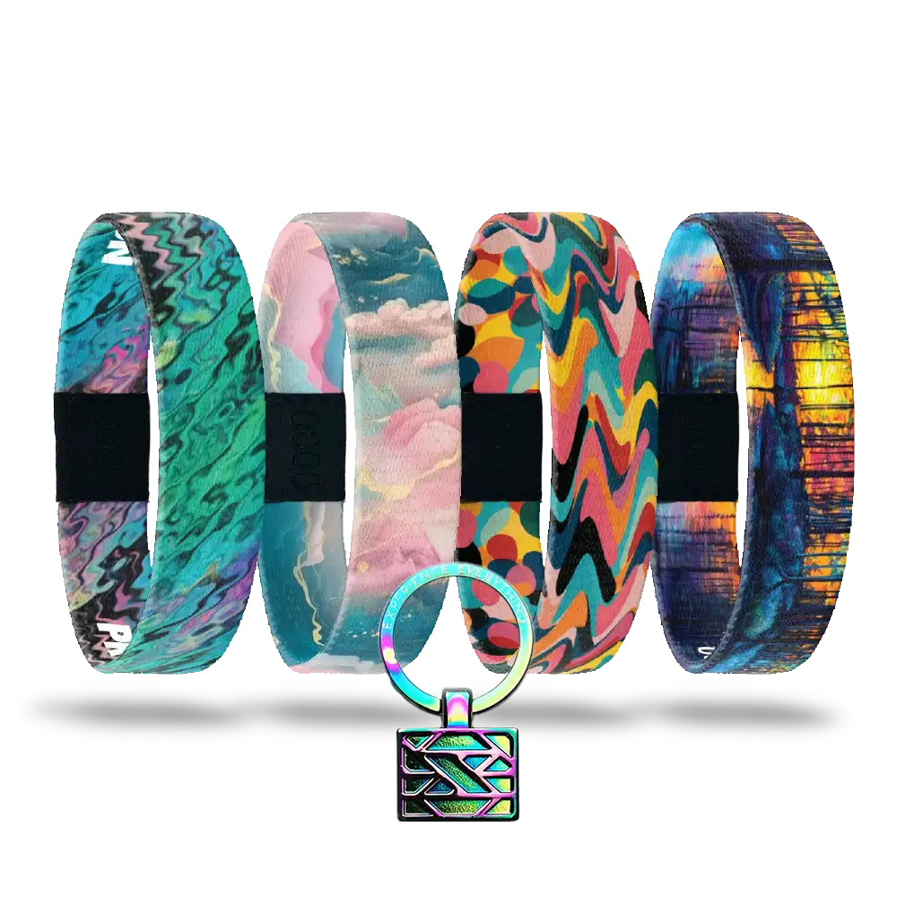The Self-Care Pack features five vibrant, patterned affirmation bracelets with unique abstract designs, arranged in a row. A small round keychain with a geometric print and metallic lock completes this inspiring set.