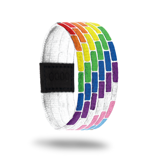 Outside is a white background which looks like a brick wall. Each level of brick is a different color of the rainbow. Inside is all white and says "PROUD" in rainbow lettering. 