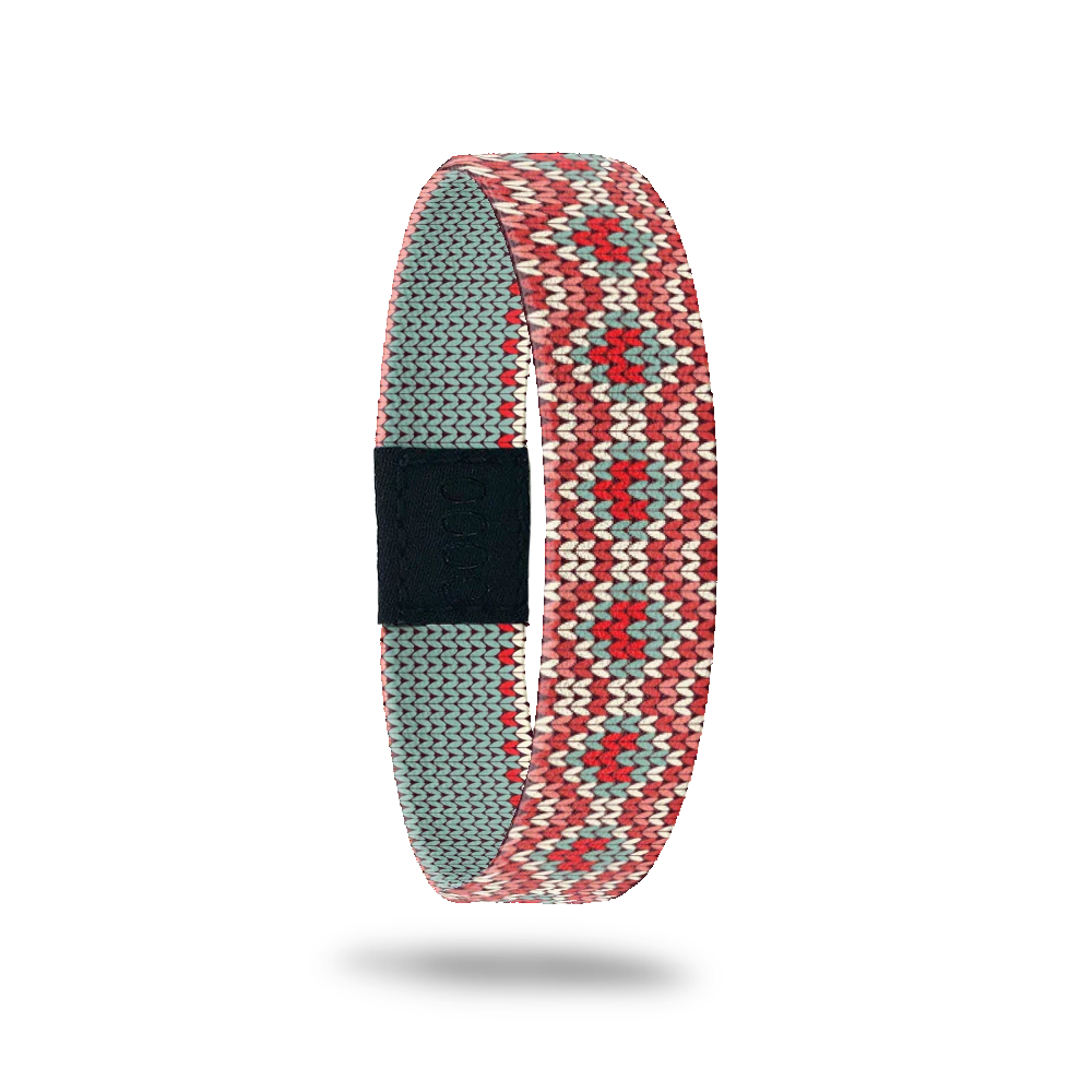 Wristband with blue, pink, taupe and light green dot design of hearts. The inside is all muted green dots and reads She Is in off white. 