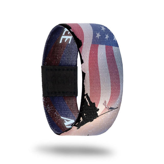 Outside design of America, The Free: United States flag in the background with faded color and black silhouette of soldiers raising a flag on a slanted pole
