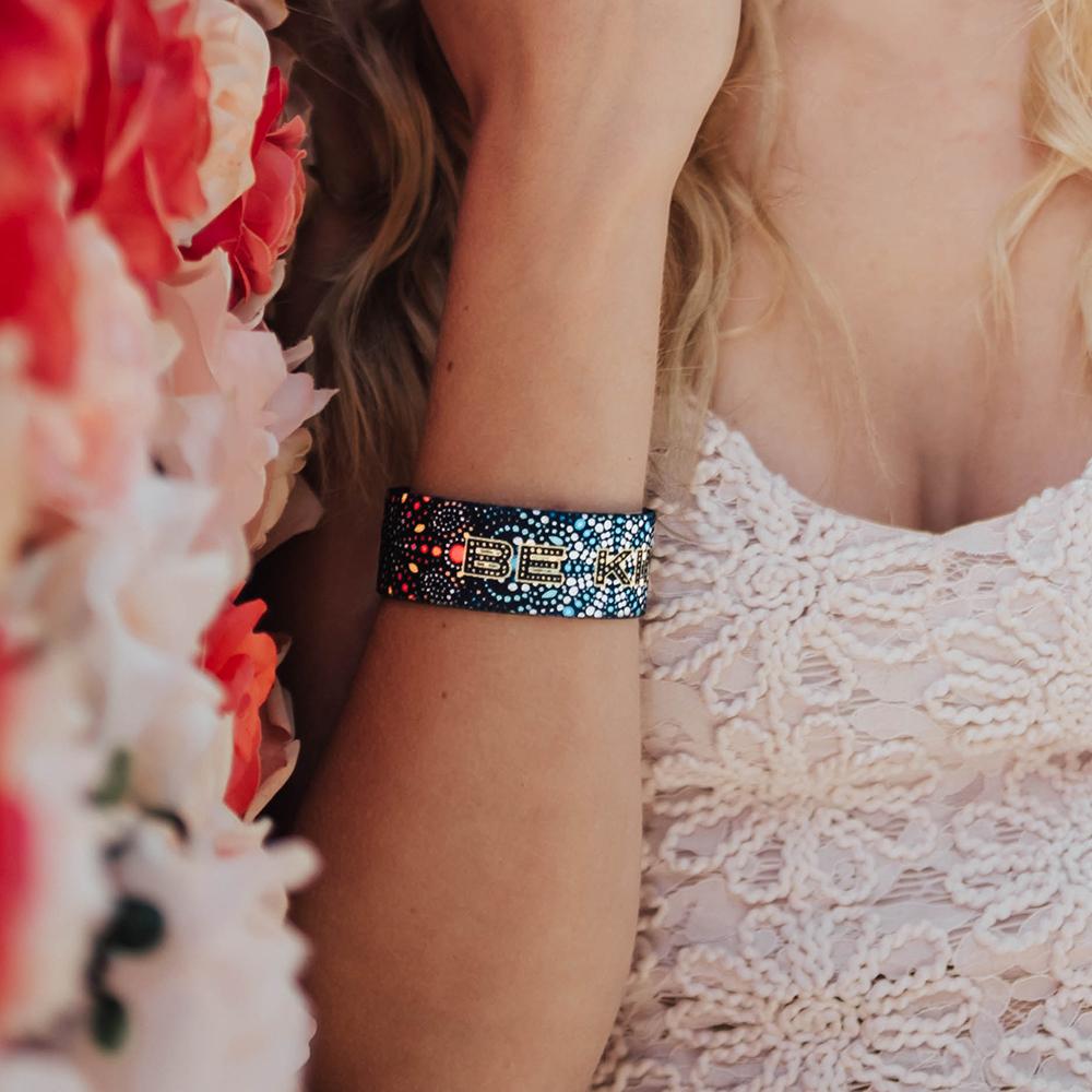 Studio Image of Be Kind on wrist next to white and pink flowers