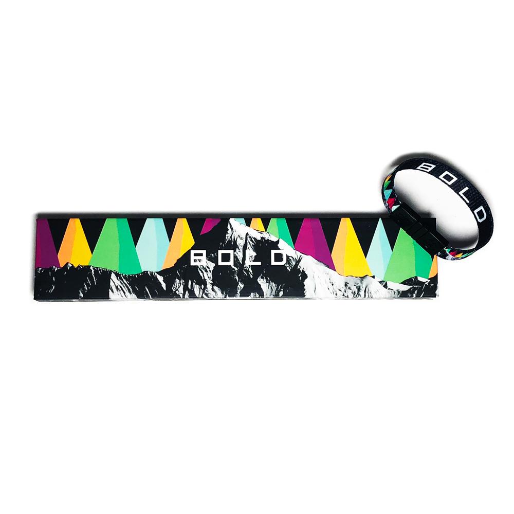 Studio image of Bold clasped together laying on the box it comes in, which has a design of colorful triangles placed next to each other like a mountain range and in front is an image of a realistic black and white mountain range.