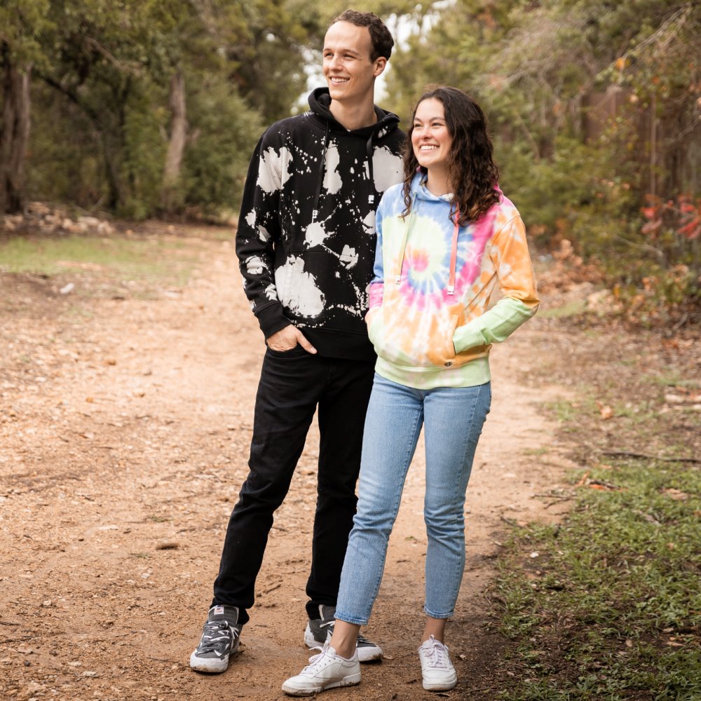 Jordan and Sarah wearing each design of hoodie, in the woods. 