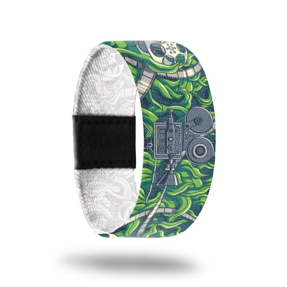 Outside design of Cinephile has a old film projector in gray at the center of the design with white and gray colored film unraveled along the design over a green grass-like background