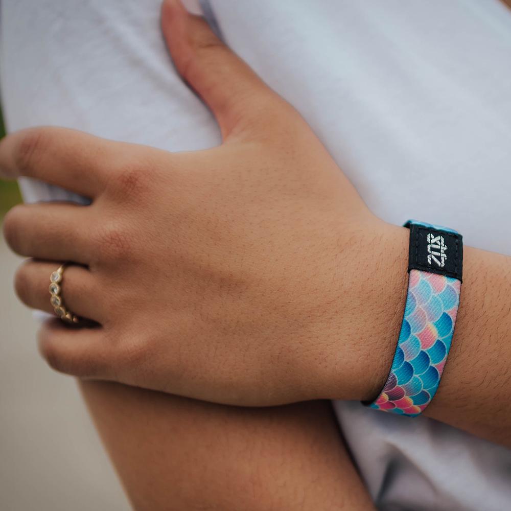 Lifestyle photo of girl's hand wearing do my best single showing the outside design with fish scales of a variety of scales of blue, coral, and purple gradient coloration