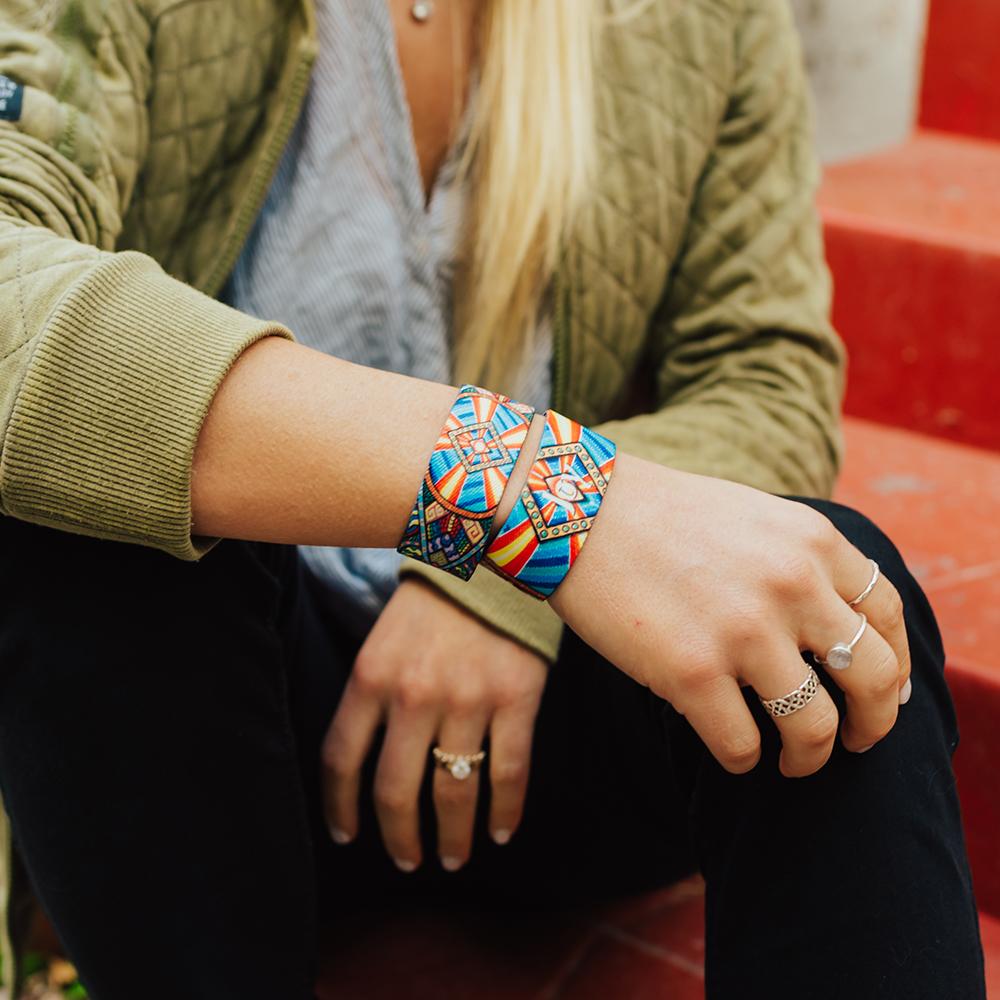 Lifestyle image close up of someone's arms crossed and resting on their legs with two Joy straps on their arm