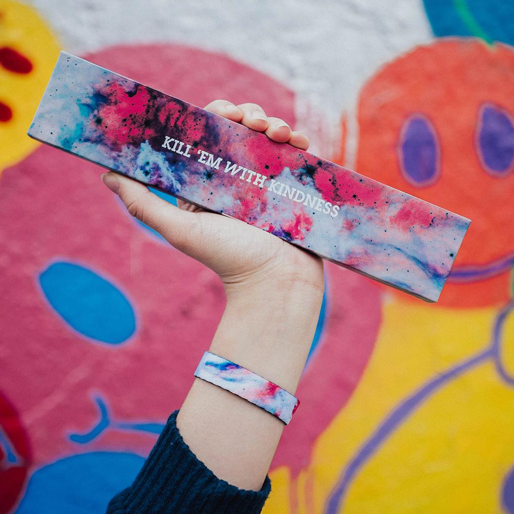 Lifestyle image of a hand holding a colorful box that says Kill 'Em With Kindness and wearing the Kill 'Em With Kindness imperial