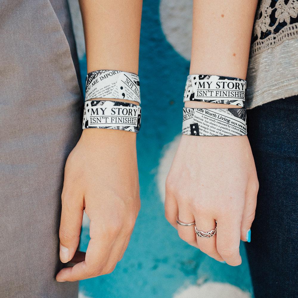 Lifestyle image close up image of two wrists both wearing 2 My Story Isn't Finished straps