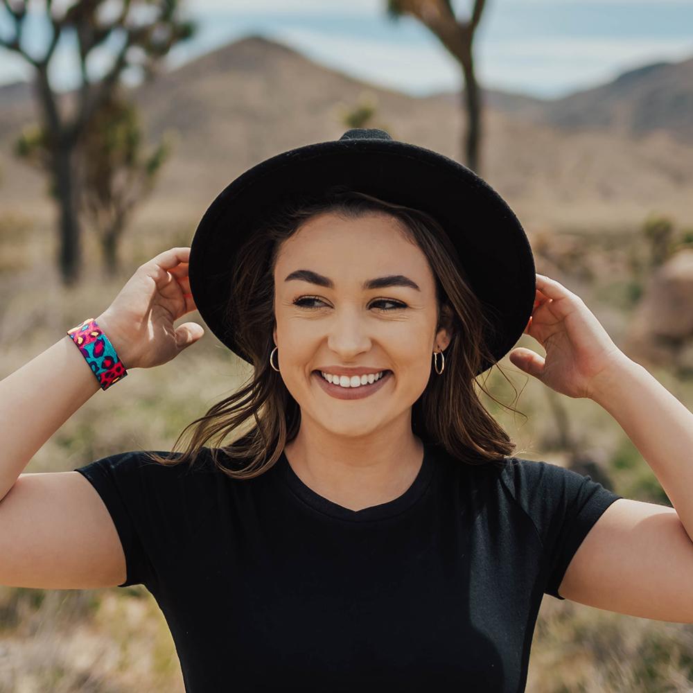 Lifestyle image of someone holding onto their hat with both hands, smiling, and My Best Self on one of their wrists