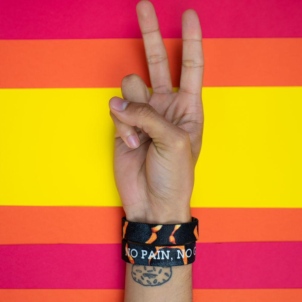 Studio photo of a hand signing a peace sign in front a bright colored background showing the inside and outside design of the no pain, no gain single