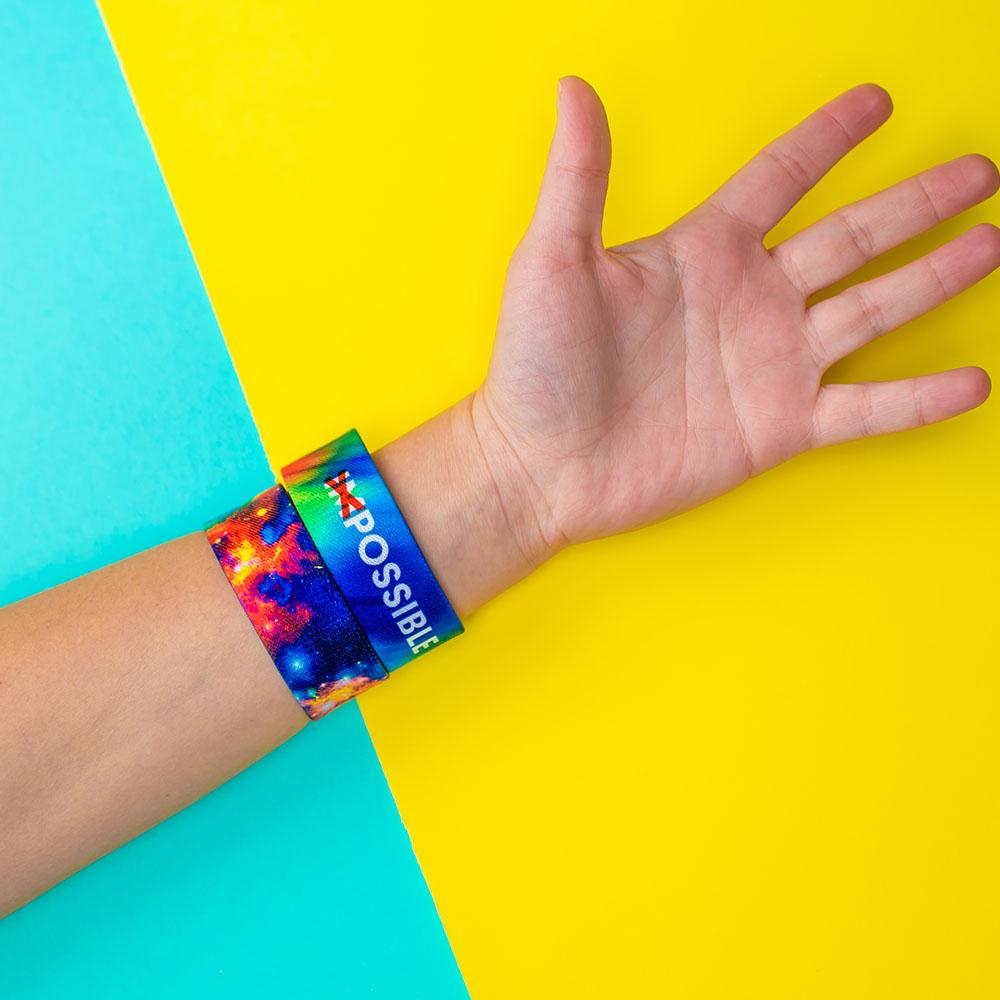 Studio image close up of 2 Possible straps on someone's wrist in front of a yellow and teal background
