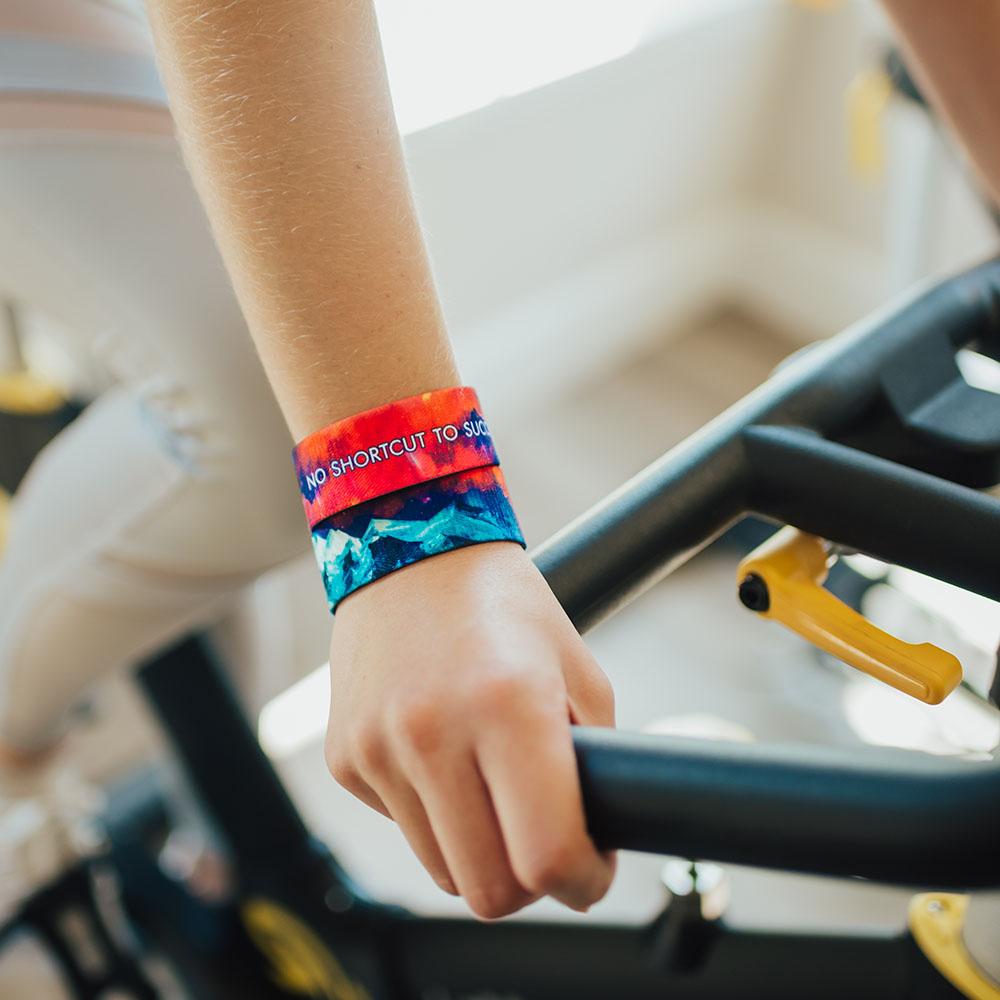 Lifestyle image of someone resting hands on an exercise bike with 2 No Shortcut To Success on wrist