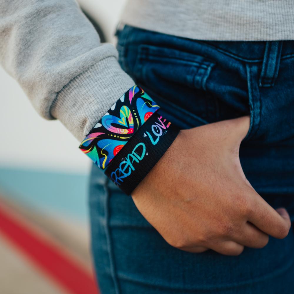 Lifestyle close up image of model's hand in their pocket and wearing two Spread Love straps 