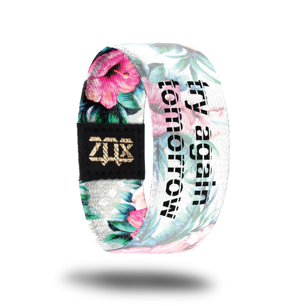 Inside design for Try Again Tomorrow. Grey with small white squares background with pink and light orange flowers and green leaves. With a transparent white over the background and flowers. Centered is Try Again Tomorrow in black text  