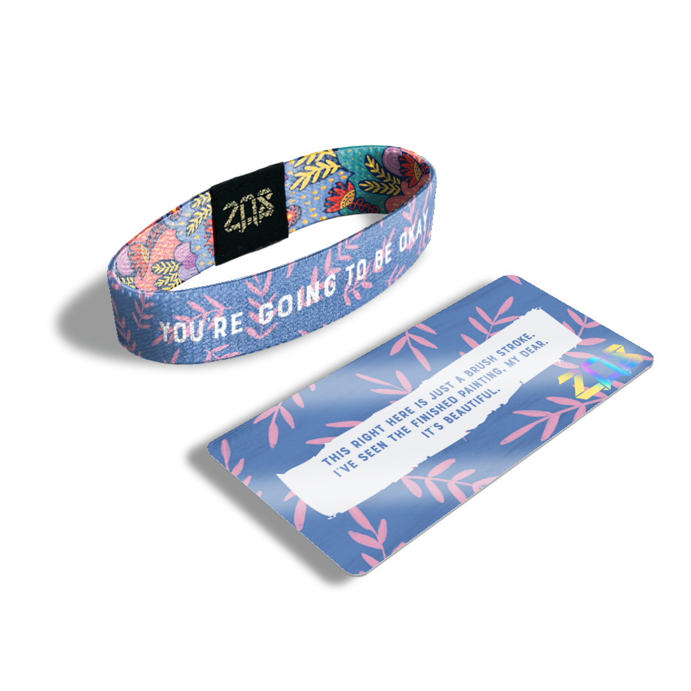 Product photo of the inside of You're Going To Be Okay. It is purple with pink leaves on branches with white text overlaying you’re going to be okay and its card saying ‘This right here is just a brush stroke. I’ve seen the finished painting, my dear. It’s beautiful.’